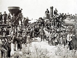 A blank and white photograph of men shaking hands by two railroad locomotives