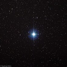 Na výřezu malé části oblohy s černým pozadím a bílými hvězdičkami v pozadí dominuje uprostřed jedna velká zářící hvězda Vega vytvářející 4 silné paprsky nahoru, dolu, doprava a doleva a zároveň je okolo ní souvislá světelná zář do všech stran, přičemž oba tyto světelné efekty sahají asi do vzdálenosti odpovídající 2,5 násobku průměru této hvězdy