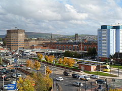 A Metrolink and bus station in front of office buildings. There are hills in the background and a road in the foreground