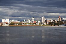 A city located on the opposite side of a large river, with a domed building in the city center.