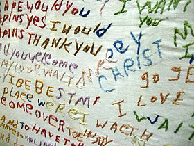 A white cloth with seemingly random, unconnected text sewn into it using multiple colors of thread