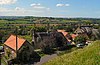 Thatched and red roofed houses along a road with a patchwork of fields behind.