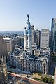 Bird's eye view of a large building with a white exterior and a tall spire; the spire has a rounded roof and is topped with a black statue.