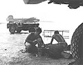 US Navy maintenance crews VB-106 clean engine parts under an airplane wing while raining at Momote Airstrip in March 1944