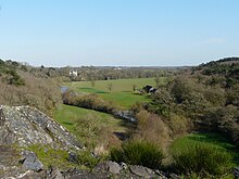 Vallée verdoyante, présentant arbres et prairies ; au fond, on distingue un châteaux blanc au toit d'ardoise.