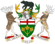 A central shield with the upper part showing the red cross of St. George and the lower part showing three golden maple leaves on a green background. There is a black bear on top of a knight's helmet above the shield with a moose to the left and a Canadian deer to the right. The province's motto "Ut incepit Fidelis sic permanet", Latin for "Loyal she began, loyal she remains" is written below the crest.