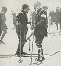 Photographie en noir et blanc d'une femme souriante et d'un homme moustachu à skis se faisant face.