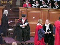 Церемония по награждаването в Оксфордския университет. Ректорът е облечен с пелерина и качулка като магистър, проктор в официална пелерина и новите доктори по философия с изцяло червени пелерини. Зад тях е глашатай, доктор, бакалаври на изкуствата и завършилите медицина