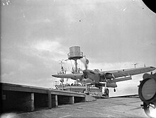 Black-and-white photograph of a single-engined monoplane running along the deck of an aircraft carrier