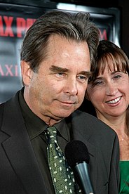 Aging Caucasian male with dark hair that is graying slightly. He is wearing a black button-down shirt and green tie.