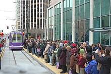 A large crowd of people on a station platform waiting for an approaching streetcar.