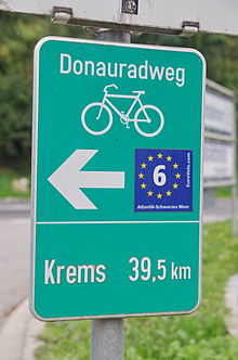 Cartel con una flecha. Indica la distancia de 39 km a Krems. Incluye una pegatina de EuroVelo 6