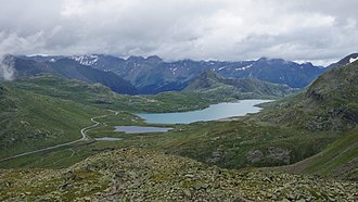 Blick aus der Diavolezza-Seilbahn zum Berninapass mit Passstrasse und Bahnlinie, Station Ospizio Bernina in Bildmitte am Lago Bianco.