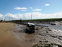 Rive boueuse avec un petit bateau. L'eau peut encore être vue dans le canal vers la droite.