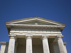 Le fronton triangulaire, la frise sculptée et les colonnes qui les supportent sont en pierre blanche.