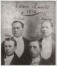 Photographie noir et blanc de quatre hommes en habit noir et plastron de concert.