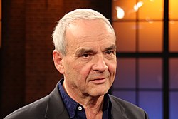 close-up of Walter Kreye wearing a dark blue shirt and black blazer, smiling slightly and looking left of camera