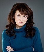 Photo of Susanne Bier standing in front of a grey wall in 2013.