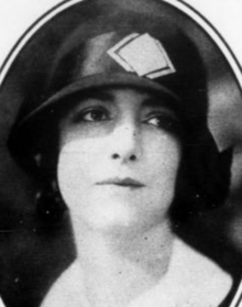 A young white woman wearing a dark cloche hat with a white diamond pattern on the band