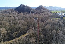 Vue aérienne d'une forêt parsemé de ruines industrielles et bordée par deux grands terrils coniques.