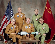 The five crew members of ASTP sit around a miniature model of their spacecraft.