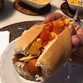 Braziliaanse hotdog met tomaat, mais, batata-palha (stroaardappelen) en ui.