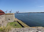 Vy från Nya Älvsborgs sydvästra bastion, Havsfrun, mot öster och Göteborg. Till vänster syns kurtin 5, med sitt skyddande fredstak. Framför kurtinen finns strandverket Stenbatteriet. Bastionen Delfins kasematterade flank syns på andra sidan om kurtinen.