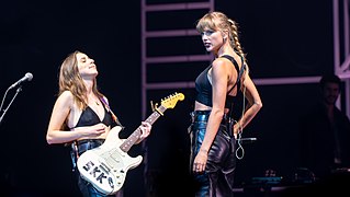 Haim and Taylor Swift in glamorous, grunge-inspired all-black outfits in a 2022 concert.