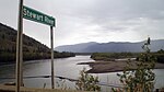 Une rivière large coule à travers les collines. Un panneau au premier plan indique "Stewart River".