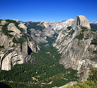 Aerial photo of wooded valley between mountain ranges against a blue sky