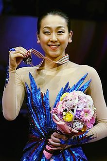 2014年世界選手権の表彰式での浅田真央の写真。左手に花束を持ち、左手で金メダルを掲げている。