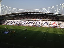 A grandstand full of people holding up coloured cards spelling out the word "Muamba" and the number 6