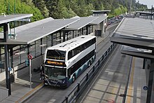 Blick von schräg oben an einer zweispurigen, überdachten und verglasten Busstation inmitten einer Autobahn. Stehender Doppelstockbus im Sound-Transit-Farbschema, Frontbeschilderung: 513 SEATTLE 5th AVE.