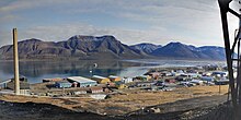 Longyearbyen with coal power plant and industrial buildings in the foreground with the fjord and bare mountains behind.