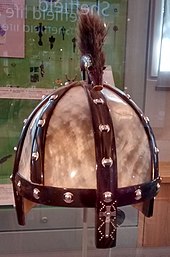 Photo d'un casque composé d'une armature en fer et de plaques de corne surmonté d'une figurine de sanglier avec de longs poils dressés