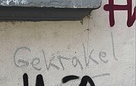 Auf einer Wand steht mit krakeliger Schrift "Gekrakel" geschrieben.