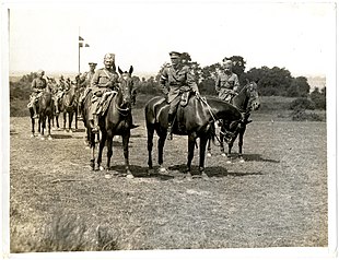 Three men on horseback in front of other mounted men