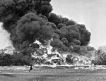 Une démonstration de fougasse incendiaire, quelque part en Grande-Bretagne, vers 1940. Une voiture est entourée par les flammes et un énorme nuage de fumée.
