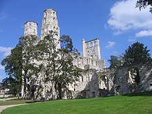 Photo des ruines d'un grand bâtiment de pierre grise avec deux hautes tours et des arches