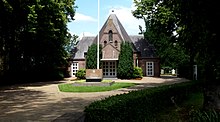 Front facade of an old cemetery building surrounded by trees with a monument in front