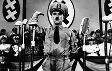 Photographie en noir et blanc tirée d'un film, où le personnage principal est habillé en dictateur levant la main dans une parodie de salut nazi.