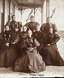 Eight women in Victorian-style dresses posing for a photo in front of a building. The woman in front and center is labeled with handwriting as "Mother Sarah Leach". The remaining seven woman form two rows behind Mrs. Leach. The three woman in the back row are also labeled in handwriting from left to right, "Mrs. Killion, Mrs. F.P. Sargent, and Mrs. E.A. Ball".