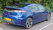 Rear 3/4 view of a dark blue automobile with trees in the background and a UK licence plate