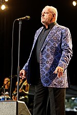 English musician Joe Cocker, standing before a microphone.