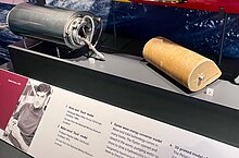 Two models of the Duck in a glass display case. One constructed of metal with cables protruding from it, the other a simpler wooden model of a similar shape. Below this is a panel with a photo of Salter and the text: 1. Wide tank 'Duck' model Edinburgh Wave Power Group, Edinburgh, Scotland, 1980s. On loan from the National Mining Museum. 2. Scotland Balsa wood 'Duck model Professor Stephen Salter, Edinburgh, Scotland 1974. On loan from the National Mining Museum Scotland.