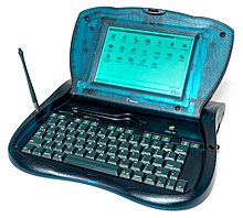 Dettaglio del retro di un computer traslucido curvo, blu-verde; sono visibili una maniglia in plastica bianca e un foro di ventilazione.