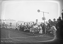 Photographie en noir et blanc d'un coureur à pied à l’arrivée d'une course, regardé par des spectateurs.