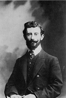 Studio portrait of a dark haired young white man, with neat beard and moustache