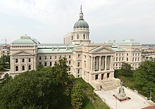 A view looking down on a large building made of limestone. It is three stories high with two wings sweeping out from a central atrium with a domed stained glass roof