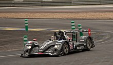 An black open cockpit LMP2 sports prototype car being driven around on a motor racing track